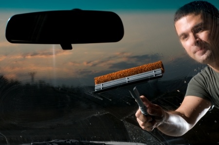 Взрослый мужчина чистит лобовое стекло своего автомобиля.